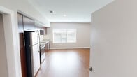 This studio unit in Cedar Park, Texas offers a thoughtfully designed open-concept layout that seamlessly blends the kitchen and living area into one cohesive space. Warm hardwood-style flooring runs throughout, complementing the neutral, light-toned walls and creating a clean, modern aesthetic.

The kitchen is a standout feature, outfitted with rich dark-wood cabinetry extending to the ceiling for ample storage, granite-style countertops, a herringbone tile backsplash, and a full suite of stainless steel appliances including a range, microwave, dishwasher, and refrigerator. A double-basin stainless steel sink and generous counter space make this kitchen both functional and visually appealing.

The open living area is bright and versatile, benefiting from a large window fitted with blinds that allows natural light to fill the room. Recessed lighting provides additional illumination throughout.

The bathroom is well-appointed with a dark wood vanity, granite countertop, a framed mirror, and a soaking tub with a tiled shower surround, finished with chrome fixtures. The overall design of this studio is modern and cohesive, making efficient use of its compact footprint while maintaining a comfortable and stylish living environment.