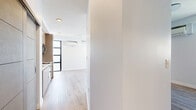 This contemporary one-bedroom, one-bathroom unit at 3279 San Marino St, Unit 506, in Los Angeles offers a thoughtfully designed layout spread across a single floor. Light-toned wood-style flooring runs throughout, creating a clean, cohesive aesthetic. The open-concept living area is a standout, featuring a dramatic full-width roll-up glass garage door that floods the space with natural light and provides direct access to outdoor views — a distinctive architectural element rarely found in urban residences. A wall-mounted mini-split system provides efficient climate control in both the living area and the bedroom. The kitchen is outfitted with flat-front cabinetry in a warm wood tone, stainless steel appliances including a gas range, microwave, and refrigerator, and a sleek countertop with an integrated sink. Large sliding barn-style doors separate the living space from the bedroom, offering flexible privacy. The bedroom is a comfortable, well-proportioned retreat with clean white walls and its own mini-split unit. A hallway connects the rooms to the full bathroom, which features wood-look flooring, crisp white walls, and a glass-enclosed walk-in shower with a herringbone tile surround. The overall design balances modern industrial elements with warm, neutral finishes throughout.