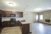 This single-floor residence is designed with a contemporary aesthetic, emphasizing an open and functional layout. The living area is bright and welcoming, featuring wood-style plank flooring, neutral gray walls, and a sleek built-in fireplace flanked by windows that allow natural light to filter in. The space flows seamlessly into the kitchen and dining area, creating an expansive, connected environment.

The kitchen is well-appointed, featuring crisp white shaker-style cabinetry, granite countertops, and a full suite of stainless steel appliances including a French door refrigerator, range, and over-the-range microwave. A central island with matching granite provides additional prep and seating space, illuminated by stylish pendant lighting overhead. Recessed lighting throughout adds to the kitchen's polished finish.

The bedrooms offer a softer feel with plush carpeting and windows overlooking greenery, providing a calm and private retreat. The bathrooms are finished with large-format tile flooring, white cabinetry, granite countertops, and generous vanity mirrors. One bathroom includes a tub-shower combination, while another features a dedicated vanity area with ample storage. The overall design is cohesive, clean, and move-in ready.
