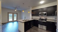 This single-story residence is designed with a modern, open-concept layout that seamlessly connects the kitchen and living areas. The kitchen serves as a central highlight, featuring dark espresso cabinetry with sleek hardware, granite countertops, and a full suite of stainless steel appliances, including a gas range, over-the-range microwave, dishwasher, and refrigerator. A peninsula with a double-basin sink and pendant lighting overhead adds both functionality and style, while wood-style flooring runs throughout the main living areas, enhancing the contemporary aesthetic.

The living area benefits from a ceiling fan and access to natural light through an exterior door. Bedroom spaces are finished with plush carpeting, ceiling fans, and windows that allow outdoor views and natural light. The bathroom includes a granite-topped vanity with dark cabinetry, a tiled tub-shower combination, wood-style flooring, and a walk-in closet area with built-in shelving. A second bathroom features a tiled tub surround and similar finishes consistent with the rest of the unit. Overall, the space presents a cohesive, neutral palette with modern finishes throughout.