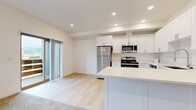 This single-floor residence offers a clean, contemporary design throughout. The kitchen serves as a central highlight, featuring crisp white shaker-style cabinetry extending to the ceiling, light quartz countertops, and a full suite of stainless steel appliances including a refrigerator, range, over-the-range microwave, and dishwasher. A peninsula island provides additional counter space and naturally separates the kitchen from the adjacent living area. Recessed lighting illuminates the space efficiently throughout.

The living area is carpeted and benefits from natural light through a window and a sliding glass door that opens to an outdoor balcony, offering views of the surrounding area. The transition between light hardwood-style flooring in the kitchen and plush carpet in the living and bedroom areas creates a clear delineation of zones.

The bedrooms are generously proportioned, each featuring soft carpet, neutral walls, and sliding closets equipped with wire shelving for storage. Windows bring in natural light, maintaining a bright and airy atmosphere. The overall design palette—white walls, light flooring, and neutral tones—creates a cohesive, move-in-ready environment throughout the entire unit.