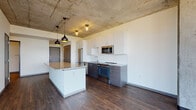 Located at 1840 N Farwell Ave in Milwaukee's vibrant East Side neighborhood, this contemporary residence showcases an industrial-modern aesthetic defined by exposed concrete ceilings and rich hardwood-style flooring throughout. The open-concept living and kitchen area is a standout, featuring a granite-topped island, two-tone cabinetry with white uppers and dark lower cabinets, a classic white subway tile backsplash, and a full suite of stainless steel appliances including a refrigerator, range, microwave, and dishwasher. Statement pendant lighting adds warmth to the industrial ceiling above. A structural concrete column anchors the living space, reinforcing the building's urban character. Floor-to-ceiling windows wrap around the living area, flooding the space with abundant natural light and offering expansive panoramic views of the Milwaukee skyline and surrounding treetops. A wall-mounted split AC unit ensures year-round comfort. The bathrooms feature wood-look flooring and include both a walk-in shower and a separate tub/shower combination. The open layout and generous proportions make this a well-appointed urban residence designed for modern living.