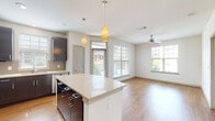 This well-appointed single-floor residence combines modern design with functional living. The open-concept layout seamlessly connects the kitchen and living area, creating a bright and airy atmosphere enhanced by abundant natural light flowing through multiple windows fitted with horizontal blinds. Light-toned hardwood flooring runs throughout the main living areas, lending warmth and continuity to the space.

The kitchen is a standout feature, anchored by a large central island with a sleek quartz countertop and stylish pendant lighting overhead. Dark espresso-toned cabinetry provides striking contrast against the light surfaces, while a full suite of stainless steel appliances — including a refrigerator, range, microwave, and dishwasher — adds a polished, contemporary edge. A tile backsplash and ample counter space complete the well-designed culinary space.

The open living area extends naturally from the kitchen, offering generous room for comfortable furnishings. A ceiling fan with a modern fixture provides both functionality and style. Bedrooms are carpeted for comfort, each benefiting from natural light and ceiling fans. The bathroom features a dark-framed vanity mirror, quartz countertop, undermount sink, and wood-toned cabinetry, offering a clean and sophisticated aesthetic. Overall, the residence presents a cohesive, modern design with quality finishes throughout.