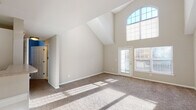 Located at The Point at Pine Ridge in Coram, NY, this multi-level residence spans three floors and offers a thoughtfully designed layout with a variety of functional spaces throughout. The living area immediately impresses with soaring vaulted ceilings and a dramatic arched window arrangement that draws in generous amounts of natural light, creating a bright and airy atmosphere. Plush carpeting and neutral-toned walls contribute to a clean, versatile aesthetic throughout the main living spaces.

The kitchen is equipped with white cabinetry, a gas range, built-in microwave, refrigerator, and tile backsplash, all complemented by warm hardwood-style flooring. The entry area also features hardwood-style flooring and a window overlooking a lush green outdoor setting, offering a welcoming transition into the home.

Bedrooms are carpeted and well-lit with natural light filtering through blinds, providing comfortable and quiet retreats. Bathrooms are finished with tile flooring, tub-shower combinations with white tile surrounds, and white vanities with large mirrors. The vaulted ceiling design continues into portions of the upper level, maintaining a sense of openness. An attached garage with an automatic opener provides convenient parking and additional storage. The wooded surroundings of Pine Ridge add a serene, natural backdrop to this well-maintained residence.