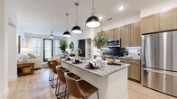 This thoughtfully designed 2-bedroom, 2-bathroom residence offers a functional and stylish single-floor layout. The open-concept kitchen and living area serves as the heart of the home, anchored by a large granite-topped island with bar seating and striking black dome pendant lights overhead. The kitchen features warm wood cabinetry, a dark tile backsplash, stainless steel appliances, and light hardwood flooring that extends throughout the main living areas. The adjacent living room is bright and inviting, with large windows allowing ample natural light, ceiling fans, and a welcoming, contemporary atmosphere. The primary bedroom offers a comfortable retreat with plush carpeting, built-in shelving, a ceiling fan, and direct access to an en-suite bathroom. The primary bathroom is well-equipped with a double granite-topped vanity, warm wood cabinetry, and a backlit mirror. The second bedroom is similarly comfortable, featuring large windows, carpet flooring, and natural light. The second full bathroom includes a granite vanity, wood cabinetry, a backlit mirror, and a tub-shower combination with decorative tile surround. Two closets and a hallway complete the layout, providing ample storage throughout this efficiently designed and stylishly finished residence.
