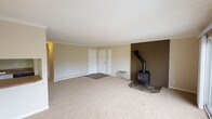 This single-floor unit offers a well-organized layout with distinct living, dining, kitchen, and sleeping areas. The spacious living room is a standout, anchored by a classic black wood-burning stove set against a full brick accent wall with a tile hearth, adding warmth and character to the space. Plush beige carpet runs throughout the living area, complemented by crown molding and a textured ceiling. A wall-mounted HVAC unit provides additional climate control. Adjacent to the living room, the dining area benefits from an abundance of natural light through large sliding glass doors that open onto a private balcony, offering views of the surrounding greenery.

The kitchen is compact and efficiently designed, featuring white cabinetry, laminate countertops, wood-style flooring, and black appliances including an electric range and a full-size refrigerator. The bedrooms are carpeted and generously proportioned, each featuring windows that allow natural light in, baseboard heating, and crown molding. One bedroom includes a closet and direct access to the kitchen area. The bathroom features a full tub-and-shower combination with white tile surround and brushed nickel fixtures, providing a clean and functional space.