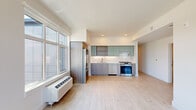 Located in Portland's Northwest District, this single-floor unit at 1985 NW Savier St offers a clean, contemporary design throughout. Light wood-tone flooring runs continuously across the space, complementing the crisp white walls and creating a bright, cohesive aesthetic.

The open-concept living and kitchen area is a functional highlight of the unit. The kitchen is outfitted with stainless steel appliances — including a gas range, dishwasher, and French door refrigerator with built-in microwave — paired with dual-tone cabinetry featuring sage green upper cabinets and warm wood-grain lower cabinets. A classic white tile backsplash and recessed lighting complete the polished look. Large windows alongside the kitchen and living area flood the space with natural light and frame views of the surrounding Portland cityscape.

The bedroom is a well-proportioned, quiet retreat with multiple windows and a sliding-door closet offering built-in shelving. A connecting hallway leads to the bathroom, which features a full soaking tub with a marble-look tile surround and brushed nickel fixtures, adding a refined touch. Throughout the unit, the design emphasizes clean lines, natural light, and practical functionality.