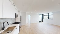 Located at 1112 Locust in Long Beach, CA, this thoughtfully designed upper-floor residence offers a clean, contemporary aesthetic throughout. Light-toned hardwood flooring flows continuously across the open-concept living and kitchen area, creating a bright and cohesive atmosphere enhanced by recessed lighting overhead.

The kitchen is well-appointed with flat-front white cabinetry, a subtle tile backsplash, and a full suite of stainless steel appliances including a gas range, built-in microwave, dishwasher, and a side-by-side refrigerator with water dispenser. The open layout connects the kitchen seamlessly to the generous living area, which benefits from abundant natural light streaming through large black-framed windows and a glass door that frames views of palm trees and the surrounding cityscape.

The bedrooms are spacious and airy, each featuring the same warm hardwood floors and black-framed windows that frame elevated views of the Long Beach skyline and neighborhood. One bedroom features a striking corner window configuration, maximizing natural light and panoramic sightlines.

Two bathrooms serve the residence, both finished with terrazzo tile flooring, white floating vanities, black-framed mirrors, and matte black fixtures. The full bath includes a tiled tub-shower combination with glass enclosure, while the second bath provides a half-bath configuration. The overall design is modern, minimal, and move-in ready.