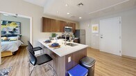 This two-bedroom, two-bathroom unit at 1055 E Tropicana in Las Vegas offers a thoughtfully designed single-floor layout that maximizes every square foot of its compact footprint. Wood-look plank flooring flows throughout the space, creating a cohesive and contemporary aesthetic.

The kitchen serves as a central hub, featuring rich walnut-toned cabinetry, white quartz-style countertops, and a full suite of stainless steel appliances including a refrigerator, electric range, microwave, and dishwasher. A peninsula with an integrated sink doubles as a breakfast bar with seating, making it both functional and social.

Each bedroom receives natural light through large windows with views of the surrounding urban landscape. The primary bedroom offers a comfortable footprint with ceiling fan, while the second bedroom includes dedicated desk space — well-suited for study or remote work. Both rooms feature wood-look flooring and neutral wall tones.

The two bathrooms are finished consistently with dark wood vanities, white quartz counters, large mirrors, and walk-in shower stalls with tile surrounds. One bathroom features accessible grab bars. The overall ambiance is clean, modern, and practical — well-suited for urban living near UNLV.