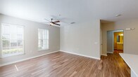 This single-floor residence offers a clean, contemporary design with warm wood-look flooring carried consistently throughout every room, creating a cohesive and inviting atmosphere. The open living area is generously proportioned, featuring neutral beige walls, white baseboards, a ceiling fan with light fixture, and a window fitted with blinds that allows natural light to filter in comfortably.

The kitchen is well-equipped with stainless steel appliances, including a full-size refrigerator, microwave, and range. White shaker-style cabinetry with brushed nickel hardware lines the walls, complemented by light countertops and a window above the cooking area. A separate layout features a peninsula-style counter that opens toward the living space, offering added functionality.

The bedrooms are bright and comfortable, each with ceiling fans, natural light from blinds-covered windows, and neutral wall tones. At least one bedroom includes a walk-in closet outfitted with built-in shelving and hanging rods. Both bathrooms mirror the kitchen's aesthetic, showcasing white shaker vanity cabinets, white countertops, large mirrors, and brushed nickel fixtures, maintaining a consistent, modern finish throughout the unit.