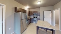 This single-floor residential unit offers a thoughtfully designed layout that balances functionality and comfort throughout its key living areas. The kitchen serves as a functional centerpiece, outfitted with a full suite of stainless steel appliances including a refrigerator, electric range, over-the-range microwave, and dishwasher. Rich, dark-toned cabinetry paired with granite-style countertops adds a polished aesthetic, while light vinyl flooring enhances the clean, modern feel. A small dining area with a granite-top table is conveniently positioned adjacent to the kitchen. The two bedrooms are finished with plush dark carpeting, neutral-toned walls, and baseboard heating units beneath windows fitted with blinds, providing a comfortable and private retreat. The bathroom is well-equipped with a full soaking tub and shower combination, a granite-top vanity with dark cabinetry, tile flooring, and direct access to a spacious walk-in closet featuring built-in shelving and hanging rods on multiple levels. A second bathroom area mirrors similar finishes, including a granite vanity and access to an additional walk-in closet. Throughout the unit, textured ceilings and neutral wall colors create a cohesive, understated ambiance suited to a variety of lifestyles.