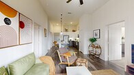 Located at 535 Main St in Nashville's 37206 zip code, this 2-bedroom, 2-bathroom unit offers a thoughtfully designed open-concept layout on a single floor. Soaring ceilings throughout lend an airy, expansive feel that goes well beyond what the footprint might suggest. The living room is bright and welcoming, anchored by a ceiling fan and large sliding glass doors that open onto a private balcony overlooking a landscaped courtyard shared by the surrounding multi-story building complex. The kitchen is a standout feature, boasting a generous island with a built-in sink, quartz-style countertops, stainless steel appliances including a range, microwave, and refrigerator, two-tone cabinetry in white and dark wood, a subway tile backsplash, and stylish pendant lighting on red cords. In-unit laundry is conveniently stacked within the kitchen area. Hardwood-style flooring runs through the main living areas. The primary bedroom is a calm retreat with plush carpet, tall ceilings, and a natural light-filled window. Its en-suite bathroom features a granite-topped vanity with dark wood cabinetry and direct access to a walk-in closet with built-in shelving. The second bedroom is equally comfortable with its own window and carpeted flooring. Two closets provide ample storage throughout the unit.