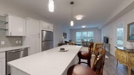 Located at 674 Dartmouth St in South Dartmouth, Massachusetts, this thoughtfully designed single-floor residence offers a cohesive blend of modern finishes and comfortable living spaces. The open-concept kitchen is a central highlight, featuring white shaker-style cabinetry, light quartz countertops with subtle veining, a subway tile backsplash, stainless steel appliances including a gas range, built-in microwave, and dishwasher, along with a generous island with bar seating. Light wood-tone flooring flows throughout the kitchen and living areas, contributing to a warm, unified aesthetic.

The living and dining areas are bright and inviting, benefiting from large windows fitted with white horizontal blinds that allow ample natural light while offering privacy. A dedicated dining nook with expansive windows provides pleasant outdoor views of the surrounding landscape.

The bedrooms are carpeted for comfort and feature classic four-poster bed frames, neutral walls, and windows with neighborhood views. One bedroom includes a built-in walk-in closet with shelving, adding practical storage.

The bathroom is finished with light wood-look tile flooring, white cabinetry, a broad vanity with a white countertop, a large mirror, and a soaking tub, creating a clean and serene atmosphere throughout.