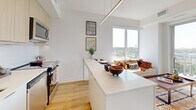 Located on the ninth floor at 610 Martin Grove Road in Toronto, this thoughtfully designed three-bedroom, two-bathroom unit offers a bright and functional layout across a single floor. The open-concept kitchen is outfitted with light wood cabinetry, white subway tile backsplash, stainless steel appliances, and a sleek white island that doubles as a dining bar with seating — all illuminated by track and pendant lighting. Warm light wood flooring runs throughout the living areas, creating a cohesive and welcoming ambiance. The living area benefits from a large floor-to-ceiling window that frames open outdoor views of the surrounding greenery and Toronto skyline. The primary bedroom is a comfortable retreat, filled with natural light and clean white walls. The two additional bedrooms each feature large windows with expansive outdoor views, providing ample natural light. Both bathrooms are finished with light wood vanities, white countertops, and neutral tile flooring — one with a tub-shower combination and the other with a walk-in shower. The unit is completed by a dedicated laundry area, a hallway with closet storage, and an overall modern aesthetic that balances practicality with clean, contemporary design.