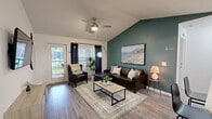 Located at 1601 SW 51st Terrace in Gainesville, FL, this single-story, 4-bedroom, 4-bathroom home offers a well-designed layout ideal for comfortable living. The living room makes a strong impression with its vaulted ceilings, ceiling fan, and wood-look flooring. A bold teal accent wall anchors the space, complemented by a wall-mounted TV, stylish furnishings, and a sliding glass door that fills the room with natural light and provides outdoor access. The four bedrooms are carpeted and individually appointed, each featuring a ceiling fan and window treatments that allow natural light to filter in. The spacious primary bedroom boasts a walk-in closet and a distinctive teal accent wall, while the additional bedrooms offer ample room for both sleeping and study areas. Each of the four bathrooms is finished with wood-look tile flooring and includes a glass-enclosed shower. Select bathrooms feature granite-topped vanities with white cabinetry and brushed gold hardware, lending a clean and modern aesthetic. A connecting hallway provides seamless flow throughout the home. The consistent use of neutral tones, modern fixtures, and accent colors creates a cohesive and inviting atmosphere throughout this well-appointed Gainesville residence.