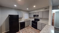 This single-story home offers a practical and cohesive layout with consistent wood-look flooring running throughout the living spaces and bedrooms, lending a warm, unified feel to the interior. The kitchen is well-equipped, featuring gray cabinetry, granite-style countertops, black appliances including a refrigerator, electric range, dishwasher, and over-the-range ventilation hood. Recessed lighting illuminates the kitchen, which also benefits from a window above the sink for natural light. The living area is open and airy, painted in a cool gray tone and accented by a ceiling fan with light fixture, creating a comfortable everyday space. The bedrooms continue the wood-look flooring theme and are painted in the same soft gray palette. Each bedroom is well-lit, with one featuring a ceiling fan and multiple windows that invite natural light, while another offers a textured ceiling and dual windows. The bathroom includes a full tub and shower combination, framed by warm earth-toned tile surround and a small window. Throughout the home, clean white trim and neutral gray walls provide a calm, move-in-ready aesthetic that is both versatile and inviting.