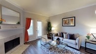 This well-appointed two-floor residence combines modern design with comfortable living across a thoughtfully arranged layout. The living area serves as a welcoming focal point, showcasing rich hardwood-style flooring that runs throughout and adds warmth to the space. Elegant crown molding frames the ceiling, lending a refined architectural detail that elevates the overall aesthetic.

Natural light pours in through a set of glass doors adorned with classic white blinds and accented by vibrant curtain panels, creating a bright and airy atmosphere. The living room offers generous proportions, comfortably accommodating a full seating arrangement centered around a sleek glass coffee table. A neutral color palette on the walls provides a versatile backdrop that complements both the furnishings and décor.

The glass doors provide a seamless connection to the outdoors, enhancing the sense of openness within the home. Subtle yet impactful design choices — including the crown molding, quality flooring, and abundant natural light — contribute to a cohesive and inviting ambiance throughout. Spanning two floors, this residence offers ample room for everyday living, with a layout designed to balance both functionality and style.