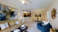 This single-floor residence offers an open-concept layout that seamlessly connects the living, dining, and kitchen areas into one cohesive and functional space. The living area is anchored by plush carpeting, crown molding, and a ceiling fan, creating a comfortable and inviting atmosphere. A large abstract wall painting adds a bold artistic touch, while ample natural light enhances the warm, neutral color palette throughout.

The kitchen features warm wood cabinetry, black appliances, and a raised breakfast bar that serves as a natural divider between the kitchen and the living space. This semi-open design allows for easy interaction between rooms while maintaining a defined cooking area.

Adjacent to the living room, the dining area is highlighted by an elegant chandelier that adds a refined touch to the space. The dining setup comfortably accommodates a full table and chairs, making it well-suited for both everyday meals and entertaining guests.

Throughout the space, consistent crown molding, neutral wall tones, and soft carpeting contribute to a cohesive and polished aesthetic. The overall ambiance is warm and welcoming, with thoughtful design details that balance everyday practicality with understated elegance.