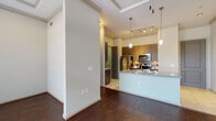 This single-floor residence showcases a thoughtfully designed open layout that balances modern finishes with comfortable living. The main living area makes a strong architectural statement with its tray ceiling, crown molding, and rich dark hardwood floors that extend throughout. Large windows and a glass-panel door flood the space with natural light and provide views of the outdoor surroundings, while a ceiling fan adds both function and style overhead.

The kitchen is a standout feature, equipped with dark wood cabinetry, a stainless steel appliance suite including a refrigerator, range, and built-in microwave, and a granite-topped island with a double sink. Pendant lighting and track lighting illuminate the workspace, while light tile flooring distinguishes the kitchen zone. A dedicated entryway with tile flooring connects seamlessly to the kitchen area.

The bedrooms offer a quieter retreat, finished with plush carpeting and large windows that bring in generous natural light. The bathroom is clean and functional, featuring a full tub-shower combination with white subway tile surround, tile flooring, and a granite-topped vanity. Throughout the residence, consistent use of granite surfaces, crown molding, and quality finishes reflects a cohesive and polished design aesthetic.