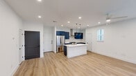 This well-designed two-story home in Leander, TX offers a thoughtful layout across two floors, with the main level housing an expansive open-concept kitchen and living area, and the upper level dedicated to three comfortable bedrooms and bathrooms. The kitchen is a standout feature, showcasing bold navy cabinetry, white subway tile backsplash, a large center island with a white quartz countertop and undermount sink, stainless steel appliances including a French door refrigerator, and a stainless wall-mounted range hood — all illuminated by stylish matte black pendant lights and recessed ceiling lighting. Light wood-tone flooring flows seamlessly throughout both levels, lending warmth and continuity to the space. The bedrooms are bright and airy, benefiting from multiple windows with exterior views and ceiling fans. The primary bedroom includes an en-suite bathroom and a walk-in closet outfitted with built-in shelving and double hanging rods. Bathrooms are clean and modern, featuring tub-shower combinations with white tile surrounds and chrome fixtures. The home's crisp white walls, clean lines, and contemporary hardware create a cohesive, move-in-ready aesthetic throughout.