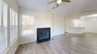 Located at 4106 Loston Ct in Fairfax, VA, this expansive single-floor home offers five bedrooms, three bathrooms, and a generously sized layout designed for comfortable living. The interior features light-toned luxury vinyl plank flooring throughout the main living areas, complemented by neutral wall tones that create a bright, airy atmosphere. The living room is a standout space, centered around a classic wood-burning fireplace with a dark surround, a ceiling fan, and a window that fills the room with natural light. Adjacent to the living area, the kitchen is outfitted with white shaker cabinetry, quartz countertops, stainless steel appliances including a refrigerator, range, and microwave, and a peninsula with a sink — ideal for both cooking and entertaining. The bedrooms are carpeted and well-proportioned, offering ample natural light through large windows. The primary bedroom is notably expansive, providing generous flexibility in furnishing and use. The three bathrooms are finished cleanly in white, featuring undermount sinks, quartz vanity tops, brushed nickel fixtures, and tub-shower combinations. A private balcony extends the living space outdoors, offering picturesque views of mature, colorful trees — particularly striking in autumn.