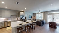 This single-story, two-bedroom, two-bathroom residence in Houston, TX offers a well-designed open-concept layout that maximizes functionality and flow. The kitchen serves as a central hub, featuring gray shaker-style cabinetry, quartz countertops with a subtle veining pattern, a full suite of stainless steel appliances including a French door refrigerator, built-in microwave, and dishwasher. A spacious island with bar seating provides an ideal casual dining or entertaining area. Adjacent built-in shelving near the entry adds convenient storage and display space.

The living area extends naturally from the kitchen and is brightened by large windows fitted with blinds and sheer drapes. A ceiling fan overhead and French doors leading to the outdoors enhance both comfort and connectivity to the exterior. Light wood-style flooring runs throughout the main living areas, lending warmth and continuity.

Both bedrooms feature plush carpet flooring and ceiling fans, with windows allowing natural light. Each bathroom is well-appointed with dual-sink vanities featuring white quartz countertops, gray cabinetry, large mirrors, and tile flooring. One bathroom includes a soaking tub with decorative tile surround and direct access to a walk-in closet, adding practical convenience to the private quarters.