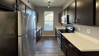 This efficiently designed 610-square-foot, one-bedroom, one-bathroom apartment is spread across a single floor and offers a well-organized layout encompassing a living room, kitchen, bedroom, bathroom, closet, and hallway. The living area features a combination of dark hardwood-style flooring and plush carpeting, complemented by vaulted ceilings that add a sense of spaciousness. Neutral gray walls throughout create a clean, modern aesthetic. The galley-style kitchen is well-appointed with dark espresso cabinetry, light quartz countertops, stainless steel appliances including a refrigerator, electric range, and microwave, plus track lighting and a window for natural light. The 130-square-foot bedroom includes plush carpeting, a ceiling fan, and a window overlooking the exterior. A separate carpeted room with a sliding glass door opens to a private balcony with views of the surrounding neighborhood. The bathroom features dark hardwood-style flooring, a combined tub and shower with a curved curtain rod, a large vanity mirror, and a dark cabinet with a marble-style countertop. A dedicated closet and hallway complete this functional and contemporary apartment.
