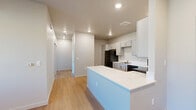 Located at 500 Stoker Ave in Reno, Nevada, this two-bedroom, one-bathroom residence offers a thoughtfully designed single-floor layout with a clean, modern aesthetic. The open-concept kitchen and living area serves as the heart of the home, featuring light wood-tone luxury vinyl plank flooring, recessed lighting, and a peninsula with white countertops that provides additional workspace and casual seating. The kitchen is well-appointed with gray shaker-style cabinetry, white countertops, a full suite of black appliances including a refrigerator, dishwasher, and microwave, and a stainless steel sink. A hallway connects the living spaces to the two bedrooms, both of which are finished with plush carpet, natural light from large windows with blinds, and individual wall-mounted climate control units. The primary bedroom is generously sized and includes a walk-in closet with wire shelving. The second bedroom features a sliding double-door closet. The shared bathroom is equipped with accessibility features including grab bars, a single-sink vanity with gray cabinetry, a large mirror, and a shower-tub combination. A dedicated laundry area adds everyday convenience to this well-planned Reno residence.