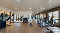 This well-appointed fitness center in Destin, Florida offers a comprehensive workout environment across a thoughtfully designed single-floor layout. The main exercise floor is expansive, featuring durable speckled rubber flooring and elevated ceilings with large ceiling fans to promote air circulation. Multiple windows along the perimeter flood the space with natural light while offering outdoor views, creating an open and energizing atmosphere.

The main floor is extensively equipped with a full rack of dumbbells, a row of cardio machines including treadmills, ellipticals, stationary bikes, and cycling bikes, as well as a functional trainer cable machine and a weight bench. Floor-to-ceiling mirrors amplify the sense of space and allow users to monitor their form. Glass doors provide convenient outdoor access and further enhance the light-filled environment.

A dedicated functional training room features rubber mat flooring and houses a rowing machine, stability balls, kettlebells, a BOSU trainer, resistance bands, wall-mounted storage racks, and a TRX-style rig — making it ideal for strength and conditioning workouts. Full-length mirrors and recessed lighting complete the room.

Adjacent to the main gym is an entry area with light wood flooring, wall art, a water station with a dual-level water fountain, and direct access to the functional training space, providing a welcoming and practical transition zone into the facility.