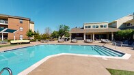 Located at 1717 Canvasback Lane in Columbus, Ohio, this single-level amenity space is centered around a generously sized resort-style swimming pool with crystal-clear blue water. The pool area is finished with a smooth concrete surround that provides ample room for lounging and entertaining. Multiple sets of plush, wicker-style outdoor seating clusters are arranged around the pool deck, offering comfortable spaces for relaxation and socializing beneath the open sky.

Adjacent to the pool, a well-appointed clubhouse building features a covered porch and large windows that allow natural light to fill the interior. The building's exterior showcases neutral siding with a classic roofline, complementing the overall aesthetic of the community. The covered patio area extends the usable outdoor space, providing a shaded retreat that connects seamlessly to the pool deck.

Mature trees and landscaping frame the perimeter of the space, adding greenery and a sense of privacy. The surrounding community buildings are visible in the background, situating this amenity area within a well-established residential setting. Overall, the space delivers a welcoming, resort-inspired atmosphere ideal for outdoor recreation and community gathering throughout the warmer months.