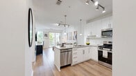Located at 75 Tresser Blvd in downtown Stamford, CT, this thoughtfully designed 2-bedroom residence offers a clean, modern aesthetic across a single floor. Light hardwood flooring runs throughout, lending warmth and continuity to every room.

The kitchen is a standout feature, outfitted with high-gloss white cabinetry reaching to the ceiling, granite countertops, and a full suite of stainless steel appliances including a gas range, built-in microwave, and refrigerator. A peninsula with seating for three, illuminated by stylish pendant lights and track lighting, connects the kitchen to the living area.

The living room is bright and airy, with sliding glass doors that open onto a private balcony overlooking greenery — filling the space with natural light and offering a seamless indoor-outdoor connection.

The primary bedroom is a comfortable retreat featuring a large picture window with views of surrounding trees and neighboring buildings. The second bedroom mirrors the clean, minimal design with its own closet and warm wood flooring.

A hallway connects all rooms efficiently, completing a layout that maximizes every inch of the space. The overall ambiance is modern and light-filled, with a neutral white palette that creates a fresh, inviting atmosphere throughout.