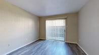 This single-story space is designed with a clean, neutral aesthetic, offering a cohesive and functional layout throughout. The living areas feature durable wood-style flooring in a cool gray tone, complementing the warm beige walls and white baseboards that are consistent throughout the home. Sliding glass doors fitted with vertical blinds appear in multiple rooms, flooding the space with natural light while providing access to the outdoors.

The kitchen is a standout feature, showcasing white shaker-style cabinetry with brushed nickel hardware, light countertops, a stainless steel sink, and a full suite of stainless steel appliances including a refrigerator, electric range, and dishwasher. The galley-style configuration maximizes efficiency while offering generous storage.

The bedrooms are finished with plush neutral carpeting and ceiling fans with integrated lighting, creating a comfortable atmosphere. Each bedroom benefits from natural light via windows with blinds. A dedicated dining area includes a pendant light fixture overhead.

The bathroom is finished with wood-look flooring, a white vanity with a single sink, a well-lit mirror, and a tub-shower combination, maintaining the home's clean and practical design throughout.
