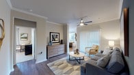 This single-floor residence is thoughtfully designed with a neutral color palette, wood-style flooring, and crown molding that flows throughout the main living areas. The living room serves as the heart of the home, featuring a ceiling fan, a bold accent wall, and a sliding glass door with vertical blinds that opens to an outdoor area, filling the space with natural light and outdoor views.

The kitchen is outfitted with dark cabinetry, white countertops, stainless steel appliances including a full-size refrigerator, and generous counter space. A dedicated dining area adjacent to the living room features large windows dressed with sheer curtains, providing a bright, inviting setting.

The bedrooms are carpeted and well-sized, each with ceiling fans and windows that bring in natural light. The primary bedroom suite includes a walk-in closet and an en-suite bathroom with dark vanity cabinetry, a large mirror, and tile flooring. A dedicated laundry room accommodates a full-size washer and dryer with shelving above.

An entryway with tile flooring provides a clean transition into the home. Throughout, the design balances functionality and comfort with consistent, modern finishes.