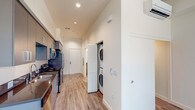 Located at 3050 Mission Inn Ave in Riverside, California, this modern single-floor unit offers a clean, contemporary design throughout. The open-concept layout is anchored by a sleek galley-style kitchen, outfitted with slate-gray cabinetry extending to the ceiling, dark countertops, and a full suite of stainless steel appliances including a refrigerator, range, and over-the-range microwave. Light wood-tone luxury vinyl plank flooring runs throughout the main living areas, lending warmth and continuity to the space. The living area is bright and open, benefiting from natural light streaming through vertical-blind-covered windows that frame views of the surrounding neighborhood. A dedicated in-unit laundry closet with a stacked washer and dryer adds everyday convenience, neatly tucked along the main corridor. The bathroom features a clean, minimalist design with a shower/tub combination, grab bar, and matching light flooring. Recessed lighting throughout the unit provides consistent, modern illumination. The overall ambiance is fresh and move-in ready, reflecting a thoughtfully designed space ideal for comfortable, low-maintenance living in the heart of Riverside.