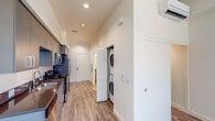 Located at 3050 Mission Inn Ave in Riverside, California, this modern single-floor unit offers a clean, contemporary design throughout. The open-concept layout is anchored by a sleek galley-style kitchen, outfitted with slate-gray cabinetry extending to the ceiling, dark countertops, and a full suite of stainless steel appliances including a refrigerator, range, and over-the-range microwave. Light wood-tone luxury vinyl plank flooring runs throughout the main living areas, lending warmth and continuity to the space. The living area is bright and open, benefiting from natural light streaming through vertical-blind-covered windows that frame views of the surrounding neighborhood. A dedicated in-unit laundry closet with a stacked washer and dryer adds everyday convenience, neatly tucked along the main corridor. The bathroom features a clean, minimalist design with a shower/tub combination, grab bar, and matching light flooring. Recessed lighting throughout the unit provides consistent, modern illumination. The overall ambiance is fresh and move-in ready, reflecting a thoughtfully designed space ideal for comfortable, low-maintenance living in the heart of Riverside.
