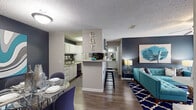 This well-appointed single-floor residence in Bellair, Florida, offers a cohesive and contemporary design throughout. The open-concept layout connects the living, dining, and kitchen areas seamlessly, creating a functional and visually engaging common space. Wood-style flooring runs through the main living areas, anchoring the bold navy and teal color palette carried throughout the unit.

The living room features a ceiling fan, sliding glass doors leading to a private patio, and ample natural light. A peninsula with bar seating bridges the living and kitchen areas, while a dedicated dining nook with a glass-top table sits nearby. The galley-style kitchen is equipped with white cabinetry, speckled countertops, black appliances, and a double sink.

Two bedrooms are finished with plush carpet and natural light from windows with blinds and curtains. Each is served by its own bathroom — both feature white vanity cabinetry, speckled countertops, large framed mirrors, and tub-shower combinations. The textured ceilings are consistent throughout, adding a classic residential touch to every room in this thoughtfully designed space.
