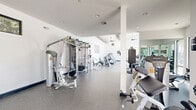 Located at 200 Bicentennial Circle in Sacramento, CA, this fitness center offers a spacious, single-floor exercise facility designed to support a comprehensive workout experience. The room is defined by soaring ceilings with exposed cylindrical ductwork and ceiling fans, lending the space an open, industrial-modern aesthetic. Floor-to-ceiling windows line one side of the room, flooding the interior with abundant natural light and providing views of palm trees and an outdoor pool area, creating an energizing and inviting atmosphere.

The exercise room is thoughtfully organized into distinct functional zones. A dedicated cardio area features a row of treadmills and elliptical machines positioned along the windowed wall, allowing users to enjoy the outdoor scenery during workouts. A separate strength training section is equipped with multi-station cable machines, weight benches, and a dumbbell rack with an accompanying mirror wall for form monitoring. The durable speckled rubber flooring throughout provides both safety and comfort underfoot.

Recessed and pendant lighting complement the natural light, ensuring the space remains bright at all times. Large glass doors provide direct access to the outdoor surroundings, enhancing ventilation and connectivity to the exterior. The clean white walls and modern equipment contribute to a professional, well-maintained environment suited for a wide range of fitness activities.