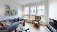 Located at 180 Friendship St in Providence, Rhode Island, this well-appointed single-floor residence offers a thoughtfully designed layout with modern finishes throughout. The kitchen is a standout feature, showcasing gray shaker-style cabinetry, stainless steel appliances including a refrigerator, range, microwave, and dishwasher, complemented by white quartz countertops, a subway tile backsplash, and a peninsula with seating for casual dining. Pendant lighting adds a refined touch overhead. Light hardwood flooring flows through the main living areas, enhancing the bright, airy atmosphere. A conveniently tucked-away stacked washer and dryer unit adds practical in-unit laundry access. The living room benefits from a bank of large windows that bring in abundant natural light and offer views of the surrounding urban streetscape. The bedroom is a serene retreat with plush carpeting, generous natural light from a well-placed window, and ample space for furnishings. The bathroom features clean, contemporary design with a glass-enclosed walk-in shower with white tile surround, a white vanity with an integrated sink, and tile flooring. Overall, the residence presents a cohesive, modern aesthetic with functional design elements suited for comfortable urban living in Providence.
