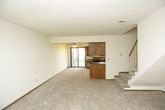 This two-story space is thoughtfully laid out across two levels, offering a comfortable and functional living environment. The main level centers around an open living area featuring plush neutral carpeting and a corner fireplace framed by a wood mantel and tile surround, creating a warm focal point. Adjacent to the living area, the kitchen is well-appointed with warm oak cabinetry, dark granite countertops, and a full suite of black appliances including a range, dishwasher, microwave, and refrigerator. A double stainless steel sink sits beneath a window, allowing natural light into the space, while a sliding glass door provides outdoor access. A built-in desk area adds a practical touch to the kitchen layout. A carpeted staircase with a wood railing leads to the upper level, where the bedrooms are located. Each bedroom features soft carpeting, ceiling fans with light fixtures, and windows that bring in natural light. The primary bedroom includes a walk-in closet and a tray ceiling detail. Bathrooms throughout the space are finished with granite-topped vanities, tile flooring, and clean white fixtures, with one offering a tub/shower combo and another featuring a standalone shower enclosure.