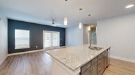 This single-story, 3-bedroom, 3-bathroom home offers a thoughtfully designed open-concept layout that maximizes comfort and functionality. The combined kitchen and living area serves as the heart of the home, featuring a large granite-topped island with an integrated sink, sleek gray shaker cabinets with gold hardware, pendant lighting, and stainless steel appliances. Light wood-look flooring runs throughout, complementing the neutral color palette accented by bold navy-blue walls in the living area. French doors bring in natural light and provide access to the outdoors, while a ceiling fan enhances airflow and comfort.

Each of the three bedrooms is well-proportioned, with large windows fitted with blinds that allow for ample natural light. The primary bedroom includes access to a dedicated closet with built-in wire shelving. Three full bathrooms are appointed with granite countertops, gray cabinetry, and tiled shower-tub combinations. Four closets throughout the home provide generous storage options, all fitted with wire rack shelving systems. A dedicated laundry room houses a full-size washer and dryer with additional wire shelving above. The home's clean, modern aesthetic and practical layout make it a highly functional living space.