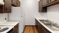 Located at 2824 Airport Hwy in Toledo, Ohio, this single-floor unit offers a straightforward and functional layout designed for comfortable everyday living. The interior is finished with neutral white walls and textured ceilings throughout, creating a clean and consistent aesthetic across all spaces.

The galley-style kitchen is efficiently arranged with dark cabinetry lining both sides, white laminate countertops, a stainless steel sink, and wood-look flooring that adds warmth to the space. A full-size refrigerator is included, and the layout maximizes storage and counter space within a compact footprint.

The living area is generously sized, featuring wall-to-wall carpeting and baseboard heating. Natural light filters in through a window flanked by a front entry door, giving the space a welcoming feel. A hallway connects the main living area to the private quarters of the unit.

The bedroom is a comfortable size, also finished with soft carpeting and equipped with baseboard heating. A window provides natural light, while two dark-toned bifold closet doors reveal a well-sized reach-in closet with a hanging rod, offering practical storage solutions.

The full bathroom features a clean white tub-shower combination, a toilet, a vanity with dark cabinetry and a wall-mounted mirror with overhead lighting, and a bright yellow vinyl floor that adds a touch of contrast to the otherwise neutral interior palette.