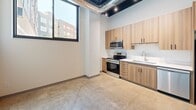 Located at 305 5th Ave S in Saint Cloud, Minnesota, this single-floor unit presents a clean, contemporary aesthetic with an industrial edge. Polished concrete floors run throughout, lending a cohesive and durable foundation to the entire space. The ceilings are notably tall, featuring exposed dark-painted ductwork and track lighting that add character and an urban, loft-inspired atmosphere.

The kitchen is efficiently designed with warm wood-toned cabinetry, white countertops, stainless steel appliances including a range and over-the-range microwave, and a single-basin sink. A large, black-framed window floods the kitchen with natural light and offers views of the surrounding neighborhood streetscape.

The hallway connects the main areas and leads to a full bathroom, which is finished with a wood-grain vanity, white countertop, undermount sink, and a large mirror — all consistent with the modern design language found throughout the unit. The remaining open areas feature crisp white walls and polished concrete floors, offering flexibility in use. Double doors provide access to a closet or storage area, adding practicality. The overall ambiance is modern, clean, and understated, well-suited for a variety of functional purposes.