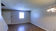 This two-floor space offers a practical and clean living environment with a straightforward design. The room pictured showcases dark, wood-style laminate flooring that provides a warm contrast against the neutral gray walls, creating a balanced and understated aesthetic. A textured popcorn ceiling adds dimension overhead, while white baseboards frame the perimeter of the room with a crisp, finished look. A single window allows natural light to fill the space, brightening the interior and contributing to an open, airy feel. The walls are smooth and move-in ready, offering a blank canvas for personalization. The overall ambiance is clean, modest, and functional, suited for everyday living. Spanning two floors, the property provides room for defined living and sleeping areas across separate levels, offering a degree of privacy and spatial separation that single-floor layouts do not provide. The no-frills design makes the space easy to maintain while still feeling comfortable and livable.