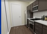 This efficiently designed 360-square-foot, one-bedroom, one-bathroom apartment offers a thoughtful layout across a single floor, making excellent use of every available square foot. The open-concept floor plan seamlessly connects the kitchen and living area, creating a cohesive and functional living space. The galley-style kitchen is outfitted with dark espresso cabinetry, white quartz countertops, a white subway tile backsplash, and a full suite of stainless steel appliances including a gas range, built-in microwave, and refrigerator — all set atop warm hardwood-style flooring that extends throughout the unit. The living area benefits from large windows that invite natural light and provide city views, complemented by recessed lighting overhead. The 120-square-foot bedroom features recessed lighting, a large window with city views, warm neutral walls, and hardwood-style flooring, offering a calm and restful retreat. The bathroom is finished with white subway tile surrounding a soaking tub with an overhead rain showerhead, paired with a dark vanity, white countertop, and light grey tile flooring. Overall, the unit presents a modern, cohesive aesthetic with a neutral color palette and quality finishes throughout.