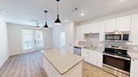 This well-designed 2-bedroom, 2-bathroom residence in Austin, TX offers a clean, modern aesthetic throughout its single-floor layout. The open-concept kitchen serves as the heart of the home, outfitted with crisp white shaker cabinetry, quartz countertops, a subway tile backsplash, and a full suite of stainless steel appliances including a range, microwave, dishwasher, and French door refrigerator. A large central island with pendant lighting overhead provides additional prep space and casual seating, while light wood-style flooring flows seamlessly throughout the entire unit. The living area connects naturally to the kitchen, with access to natural light through front-facing windows and a glass door entry. Both bedrooms are bright and well-proportioned, featuring windows with blinds that allow for ample natural light and views of the surrounding neighborhood. Each bedroom is served by its own dedicated bathroom, both finished with white cabinetry, quartz-topped vanities, framed mirrors, and glass-enclosed walk-in showers. Two closets provide convenient storage, and a welcoming entrance completes the layout. The consistent use of white walls, light flooring, and black hardware accents gives the entire space a cohesive, contemporary feel.