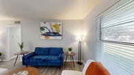 This thoughtfully designed single-floor residence offers a practical and comfortable layout across six distinct spaces, including a living room, dining room, bedroom, office, kitchen, and bathroom — all connected by a central hallway. The living room features light wood-style flooring, a textured ceiling, and a bright window with slatted blinds that allows natural light to fill the space, creating a warm and inviting ambiance. The adjoining dining area is highlighted by a large sliding glass door that opens to an outdoor patio, flooding the space with additional light and providing outdoor access. The kitchen is efficiently laid out with gray cabinetry, white countertops, and full-size appliances. The dedicated office space includes a window with natural light and ample room for a functional work area. The bedroom is a comfortable retreat, complete with a ceiling fan, a closet, and soft, neutral tones that contribute to a restful atmosphere. The bathroom features a wide vanity with a white stone countertop, under-mount sink, gray cabinetry, and a well-lit mirror framed by pendant lighting. Wood-style flooring flows consistently throughout, tying the home together with a cohesive, modern aesthetic.