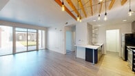 Located at 719 Virginia Ave in Indianapolis's vibrant Fountain Square neighborhood, this 2-bedroom, 1-bathroom residence blends modern design with warm architectural character. The open-concept living and kitchen area is a standout, featuring exposed natural wood ceiling beams and Edison bulb pendant lighting that create an industrial-chic ambiance. Light wood-look flooring runs throughout the main living space, complementing the bright white walls and abundant natural light from a large sliding glass door that opens to an outdoor patio area. The kitchen is well-appointed with dark cabinetry, stainless steel appliances including a range, microwave, and refrigerator, sleek white countertops, open shelving, and a textured tile accent wall. A peninsula with bar-height seating connects the kitchen to the living area. The bedrooms are carpeted for comfort, with natural light provided by windows. A clean, carpeted hallway connects the private quarters. The full bathroom features wood-look flooring, a soaking tub with shower, a dark-cabinetry vanity with white countertop, and clean white walls. A dedicated closet provides additional storage. Recessed lighting and contemporary hardware complete the polished, modern aesthetic throughout.