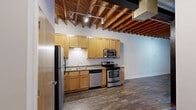 Located at 1300 Convention Plaza in downtown St. Louis, Missouri, this urban loft-style unit showcases an open, industrial-inspired design that blends raw architectural elements with modern finishes. The main living area is defined by striking exposed concrete coffered ceilings with visible structural beams and large silver ductwork running overhead, creating a distinctive warehouse aesthetic. Warm hardwood flooring extends throughout the open-plan space, complementing the bright white walls and contributing to an inviting ambiance. A wall of sliding glass doors floods the living area with natural light and provides direct access to a private balcony with views of the surrounding urban landscape.

The kitchen is thoughtfully appointed with honey-toned wood cabinetry, granite countertops, a stainless steel refrigerator, range, microwave, and dishwasher, all set beneath the same exposed ceiling structure that continues throughout the unit. The open layout allows the kitchen to flow seamlessly into the generous living area. A separate bedroom offers a quiet retreat, also featuring hardwood floors and the signature exposed ceiling detail.

The bathroom is clean and functional, featuring a full tub-shower combination with tiled surround and tile flooring. Throughout the unit, the interplay of industrial architecture and contemporary finishes creates a dynamic, urban living environment well-suited for those seeking character and style in the heart of St. Louis.