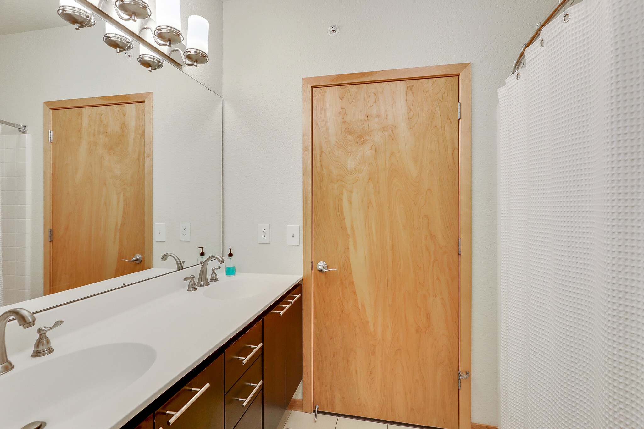 Modern bathroom with double vanity, wood door, and shower curtain.