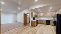 This single-floor, 2-bedroom, 1-bathroom unit offers a practical and comfortable layout across a generously sized floor plan. The kitchen is a standout feature, equipped with an abundance of light wood cabinetry, light granite-style countertops, and a full suite of black appliances including a range, over-the-range microwave, dishwasher, and refrigerator. Light hardwood-style flooring runs throughout the kitchen and living areas, contributing to a clean, cohesive aesthetic. Vaulted ceilings in the main living and kitchen area add a sense of openness and volume to the space.

The primary bedroom is a comfortable size, featuring plush carpeting, recessed lighting, and a large sliding door with vertical blinds that allows natural light to fill the room. The second bedroom also features carpet flooring, neutral walls, and a window with wood-trimmed blinds. Both bedrooms are well-proportioned and functional.

The bathroom includes a full tub-shower combo, toilet, and vanity with wood cabinetry, all set on hardwood-style flooring. A built-in shelving closet adjacent to the bathroom provides added storage. Additional storage is available through two dedicated closets, and an in-unit laundry area is conveniently accessible via the hallway.